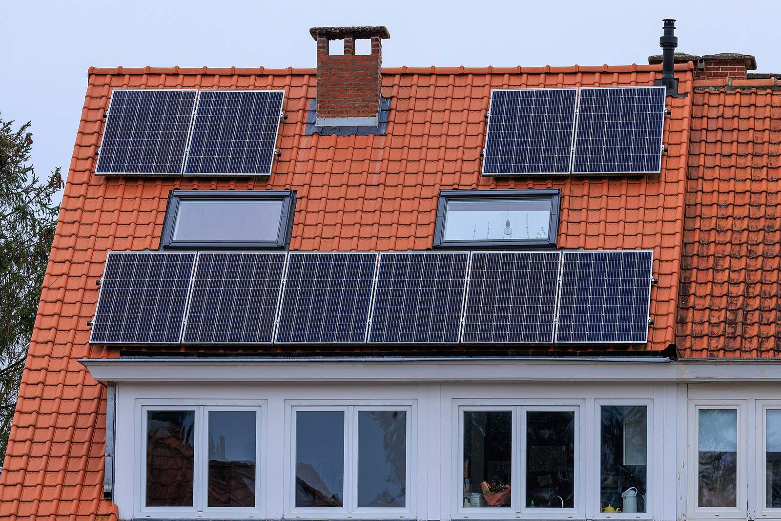 Oranje pannendak met tien zonnepanelen in drie groepen rond twee dakvensters en een bakstenen schouw