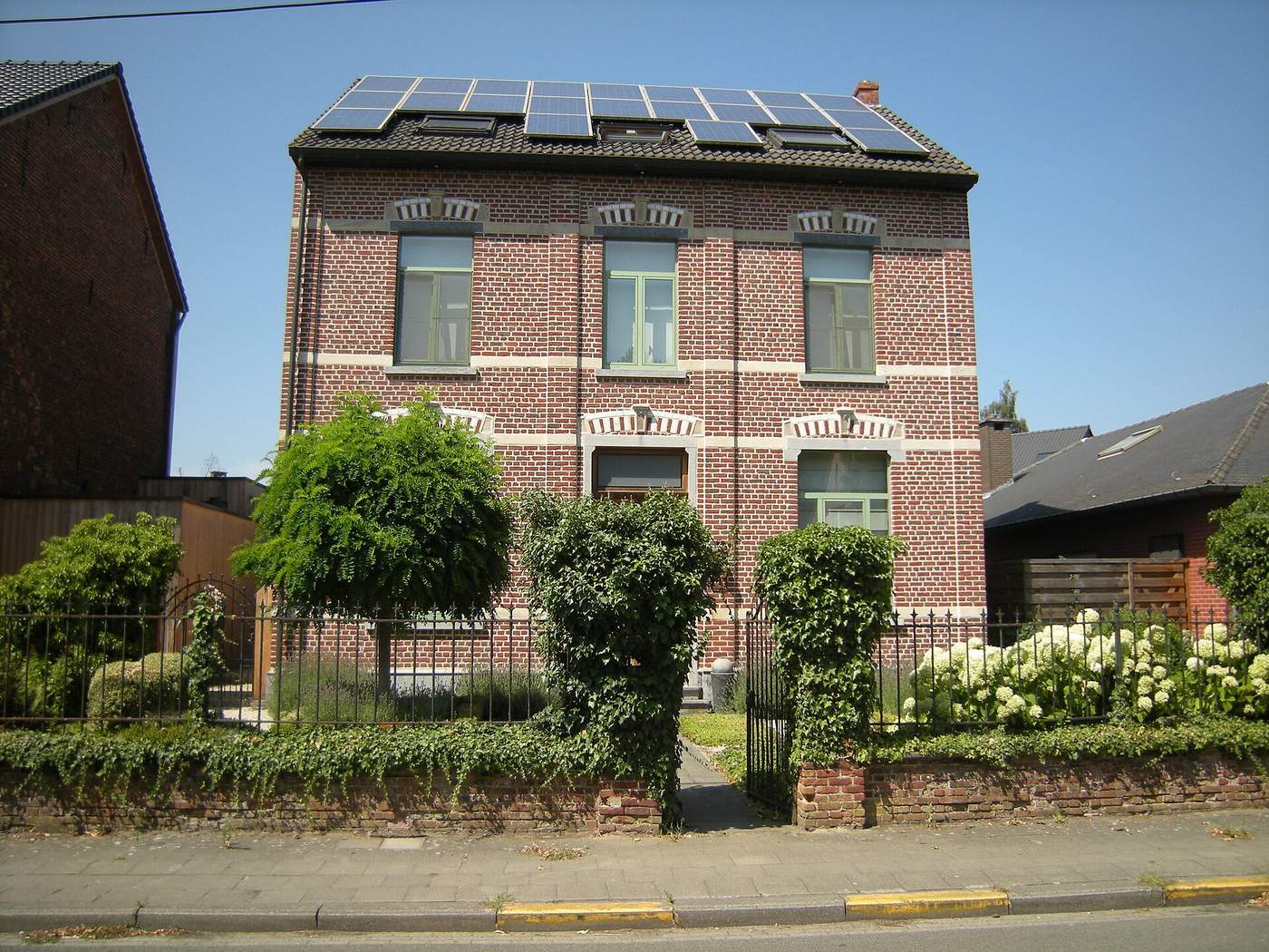 Herenhuis in rode baksteen met witte banden en zonnepanelen op het dak, achter een voortuin met hortensia's