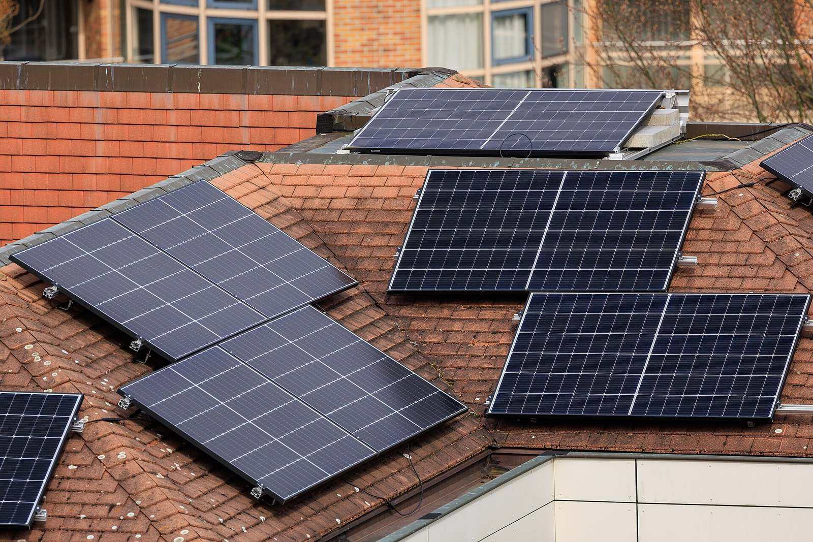 Zonnepanelen op aluminium montagerails, verdeeld over de schuine vlakken en een plat deel van een rood pannendak